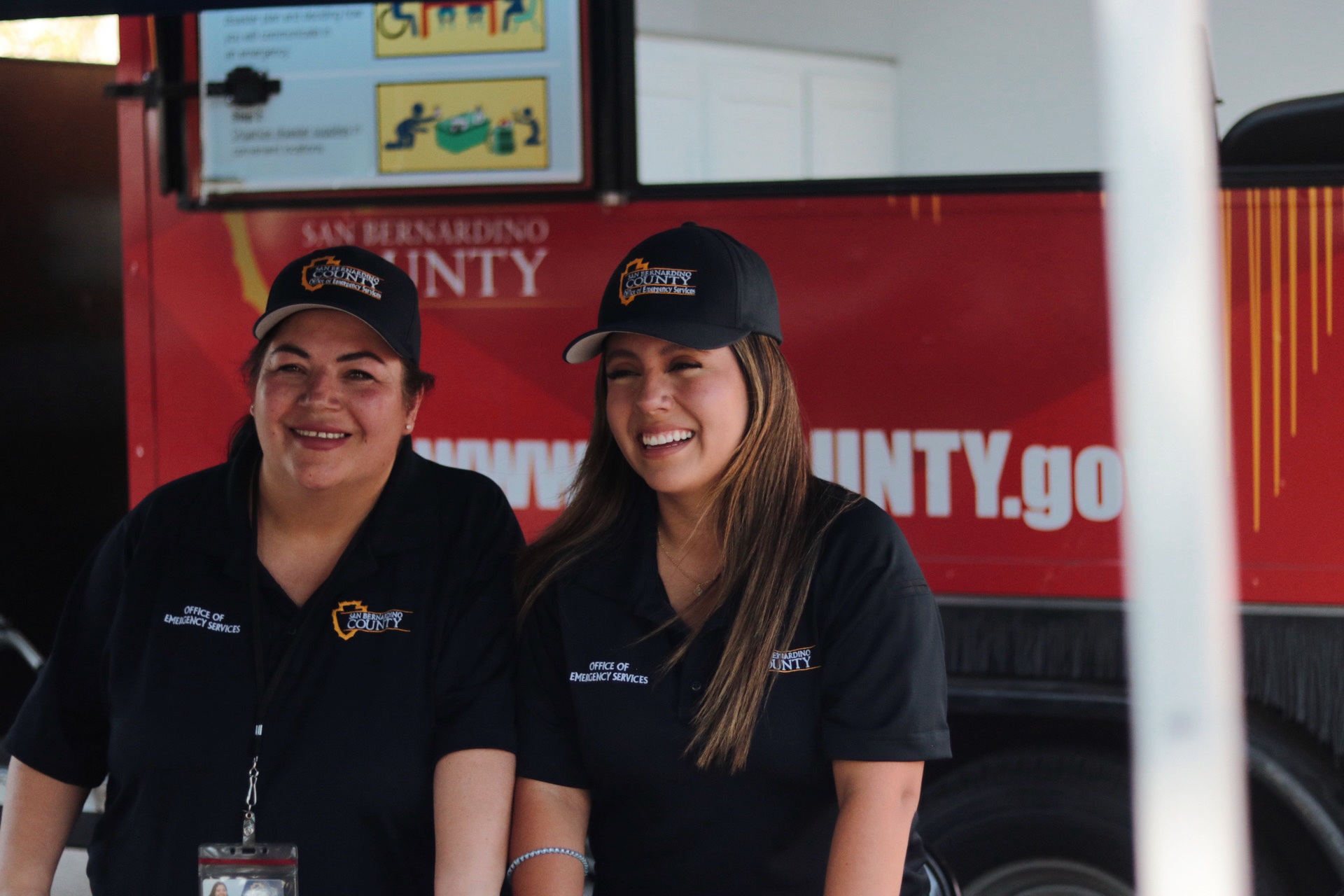 2 ladies smiling In front of earthquake simulator with office of emergency services unifrom