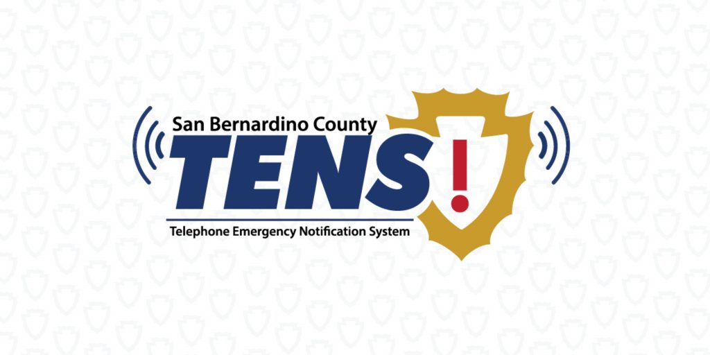 San Bernardino County Telephone Emergency Notification System (TENS) logo centered on a light gray background with a subtle shield pattern. The logo features the word “TENS” in blue, a gold shield with a red exclamation point, and blue signal wave icons on both sides.